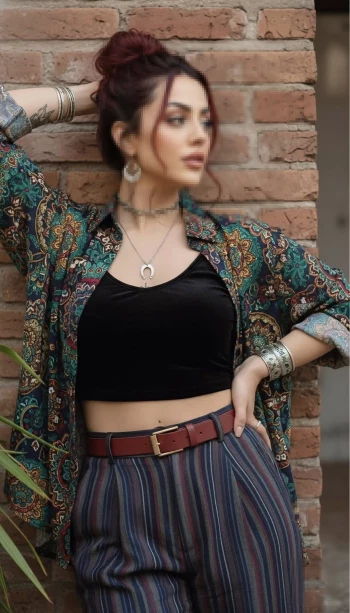 Woman posing in a patterned shirt and striped pants against a brick wall