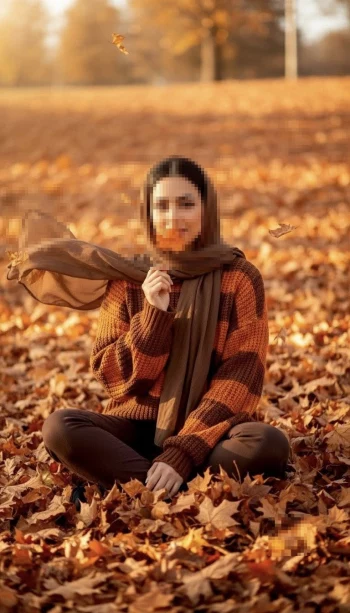 Woman sitting in autumn leaves wearing brown hijab and cozy striped sweater