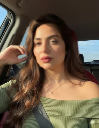 Woman sitting in car wearing olive green off-shoulder top in warm sunlight