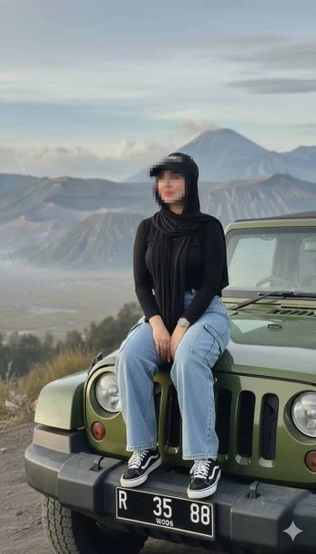 Woman sitting on green jeep with mountain view in the background
